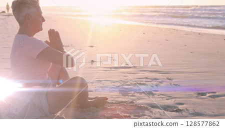 Image of light spots over caucasian woman practicing yoga at beach and meditating 128577862