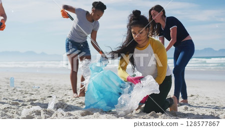 Image of globe icons over diverse female volunteers picking up rubbish on beach 128577867