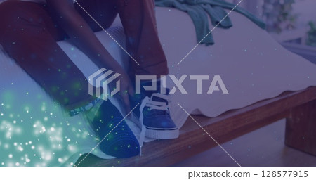 Image of lights over feet of african american boy tying shoe on bed 128577915