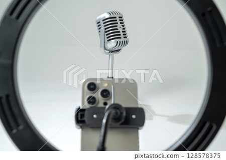 Round LED ring light with a cellphone on a phone holder with a vintage silver microphone with a white background. Vlogging or live streaming equipment. Mockup or Copy space Round LED ring light with a cellphone on a phone holder with a vintage silver microphone with a white background. Vlogging or live streaming equipment. Mockup or Copy space 128578375