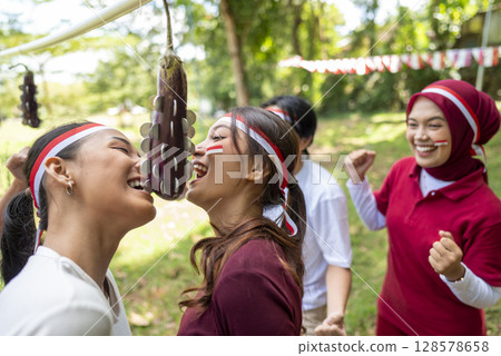 Portrait of an Indonesian southeast asian people celebrate Indonesia Independence Day on the 17th of August with a game of biting coins in eggplant outdoors. Concept of Kemerdekaan Indonesia Portrait of an Indonesian southeast asian people celebrate Indonesia Independence Day on the 17th of August with a game of biting coins in eggplant outdoors. Concept of Kemerdekaan Indonesia 128578658