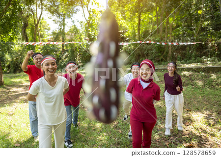 Portrait of an Indonesian southeast asian people celebrate Indonesia Independence Day on the 17th of August with a game of biting coins in eggplant outdoors. Concept of Kemerdekaan Indonesia 128578659