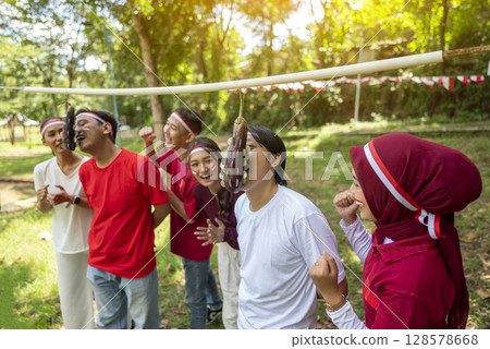 Portrait of an Indonesian southeast asian people celebrate Indonesia Independence Day on the 17th of August with a game of biting coins in eggplant outdoors. Concept of Kemerdekaan Indonesia Portrait of an Indonesian southeast asian people celebrate Indonesia Independence Day on the 17th of August with a game of biting coins in eggplant outdoors. Concept of Kemerdekaan Indonesia 128578668