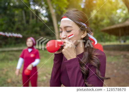 Portrait of an Indonesian southeast asian people celebrate Indonesia Independence Day on the 17th of August with a game of blowing the balloons outdoors. Concept of Kemerdekaan Indonesia Portrait of an Indonesian southeast asian people celebrate Indonesia Independence Day on the 17th of August with a game of blowing the balloons outdoors. Concept of Kemerdekaan Indonesia 128578670