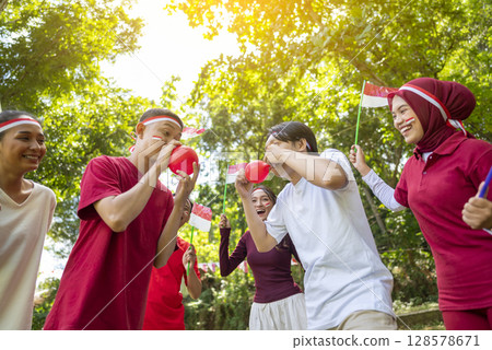 Portrait of an Indonesian southeast asian people celebrate Indonesia Independence Day on the 17th of August with a game of blowing the balloons outdoors. Concept of Kemerdekaan Indonesia 128578671