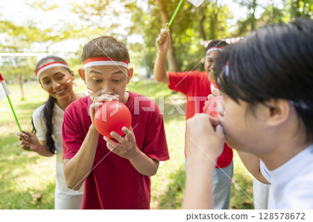 Portrait of an Indonesian southeast asian people celebrate Indonesia Independence Day on the 17th of August with a game of blowing the balloons outdoors. Concept of Kemerdekaan Indonesia 128578672