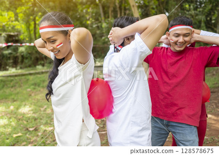 Portrait of an Indonesian southeast asian people celebrate Indonesia Independence Day on the 17th of August with a game of keep the balloon from blowing out outdoors. Concept of Kemerdekaan Indonesia Portrait of an Indonesian southeast asian people celebrate Indonesia Independence Day on the 17th of August with a game of keep the balloon from blowing out outdoors. Concept of Kemerdekaan Indonesia 128578675
