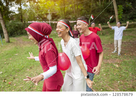 Portrait of an Indonesian southeast asian people celebrate Indonesia Independence Day on the 17th of August with a game of keep the balloon from blowing out outdoors. Concept of Kemerdekaan Indonesia Portrait of an Indonesian southeast asian people celebrate Indonesia Independence Day on the 17th of August with a game of keep the balloon from blowing out outdoors. Concept of Kemerdekaan Indonesia 128578679