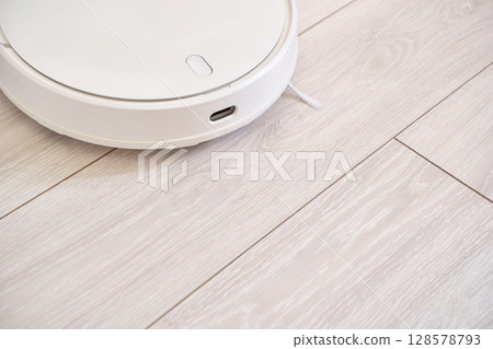 Modern white robotic vacuum on light wood floor in minimalist home setting Modern white robotic vacuum on light wood floor in minimalist home setting 128578793
