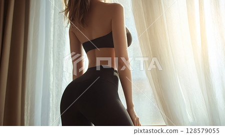 Slim sporty woman wearing black sportswear standing near window at home Slim sporty woman wearing black sportswear standing near window at home 128579055