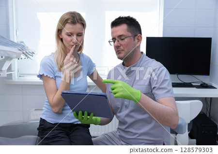 Engaging Dental Consultation: A Patient's Insightful Discussion with a Dentist Using a Tablet in a Modern Clinic Environment 128579303