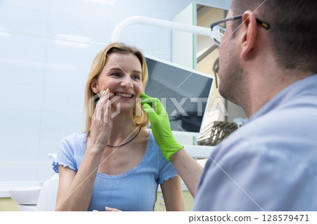 Happy dental check-up experience: A dentist smiling and counseling a patient in a modern office with high-tech equipment, both individuals radiating positivity and trust. 128579471
