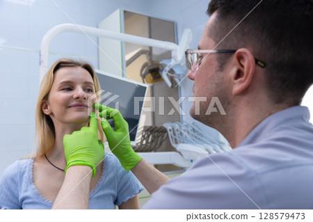 A Dentist Evaluates a Patient's Facial Structure During a Dental Consultation in a Modern Clinic Featuring Advanced Equipment and a Relaxed Atmosphere for Oral Health Care 128579473