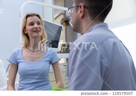 A Young Woman Engaging in Conversation with a Dentist in a Modern Dental Office Setting, Showcasing Professionalism and Patient Comfort During a Dental Visit 128579507