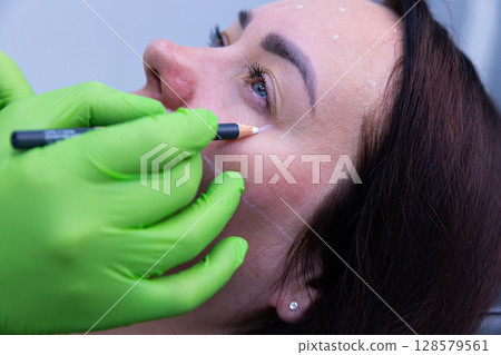 Aesthetic Procedure in Progress: Precise Marking for Cosmetic Enhancement Using Professional Techniques and Equipment by a Skilled Technician with Protective Gear Aesthetic Procedure in Progress: Precise Marking for Cosmetic Enhancement Using Professional Techniques and Equipment by a Skilled Technician with Protective Gear 128579561