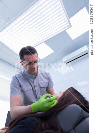 A Cosmetic Procedure in Progress: A Healthcare Professional Administering Treatment to a Patient with Care and Precision in a Bright Clinic Environment A Cosmetic Procedure in Progress: A Healthcare Professional Administering Treatment to a Patient with Care and Precision in a Bright Clinic Environment 128579567
