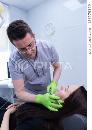 Professional Aesthetic Procedure in a Modern Clinic: Practitioner Attending to Patient with Gentle Care and Precision Using Advanced Tools Professional Aesthetic Procedure in a Modern Clinic: Practitioner Attending to Patient with Gentle Care and Precision Using Advanced Tools 128579569
