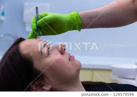 Professional Beauty Treatment Focused on Microblading Preparation with a Careful Artist Drawing Eyebrow Shape for Client in Modern Salon Space Professional Beauty Treatment Focused on Microblading Preparation with a Careful Artist Drawing Eyebrow Shape for Client in Modern Salon Space 128579599