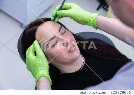Professional Approach to Beauty: An Expert Aesthetician Applies Precise Marks for an Upcoming Facial Treatment on a Calm Patient in a Modern Clinic Setting Professional Approach to Beauty: An Expert Aesthetician Applies Precise Marks for an Upcoming Facial Treatment on a Calm Patient in a Modern Clinic Setting 128579600