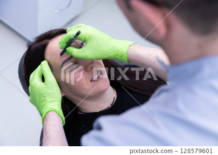 A Client Receiving Professional Eyebrow Shaping Through Precision Techniques from a Skilled Aesthetician in a Modern Beauty Salon Environment 128579601