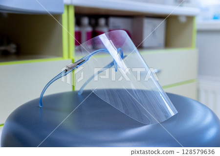 Protective Face Shield Displayed on a Sleek Gray Office Chair in a Modern Medical Facility Environment for Enhanced Safety and Health Precautions 128579636