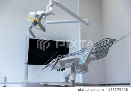 Modern Dental Treatment Room Featuring Advanced Equipment Including a Dental Chair, Overhead Light and Monitor for Patient Care and Comfort During Procedures 128579698