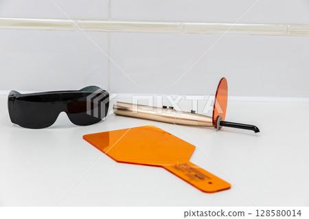 Innovative Dental Equipment Displayed on a Clean Surface: Protective Glasses, Orange Shields, and a Modern Tooth Whitening Device for Professional Use in Dental Care Settings 128580014
