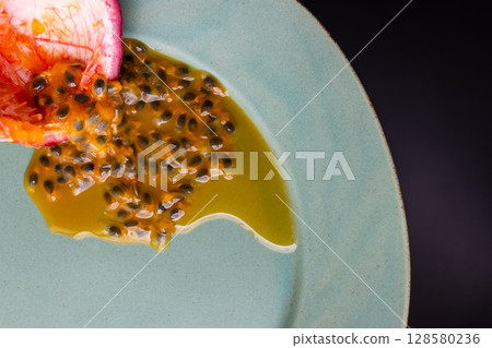 Half a passion fruit on a plate with fruit and juice spilling out Half a passion fruit on a plate with fruit and juice spilling out 128580236