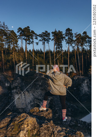 A woman in sportswear sitting on a rock at sunset, wearing a hat and looking like a hiker. The warm summer light and natural setting evoke themes of adventure, travel, and outdoor freedom. A woman in sportswear sitting on a rock at sunset, wearing a hat and looking like a hiker. The warm summer light and natural setting evoke themes of adventure, travel, and outdoor freedom. 128580302