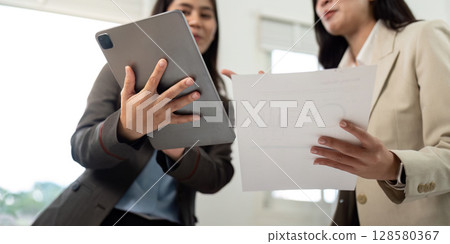Collaboration and Success. Two businesswomen discussing project details with tablet and documents. 128580367