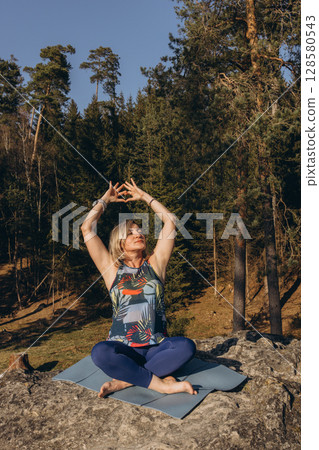 A woman meditating and practicing yoga on top of a rock at sunset, embracing wellness, mindfulness, and eco-friendly living 128580543