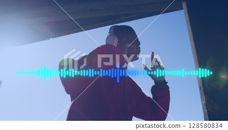 Image of soundwaves over african american man in headphones exercising outdoors in sun 128580834