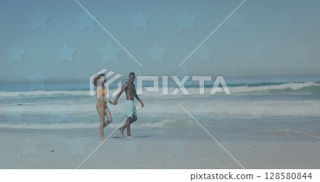 Image of stars over happy african american couple walking on beach 128580844