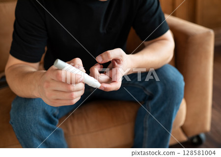 Man checking blood sugar level using a glucometer at home, focusing on hands and device. 128581004