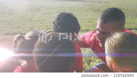 Image of light spots over diverse schoolchildren teaming up with coach at stadium 128582084