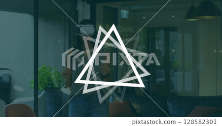 Image of triangles rotating over caucasian woman wearing vr headset in office 128582301