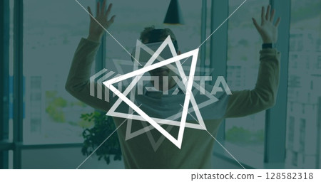 Image of triangles rotating over caucasian man wearing vr headset in office 128582318
