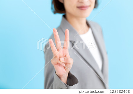 A middle-aged female business woman wearing a gray suit holding up three fingers 128582468