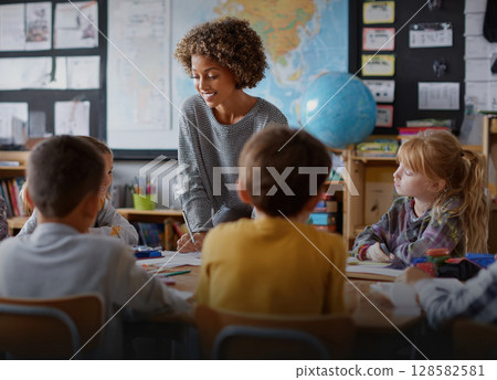 A smiling teacher interacts with elementary school students in a classroom, promoting active learning and engagement. Ideal for education, youth, and mentorship themes A smiling teacher interacts with elementary school students in a classroom, promoting active learning and engagement. Ideal for education, youth, and mentorship themes 128582581