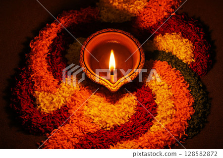 Oil lamp on colorful flower petals, creating traditional rangoli design, symbolizing warmth and light during Indian festival celebration. 128582872