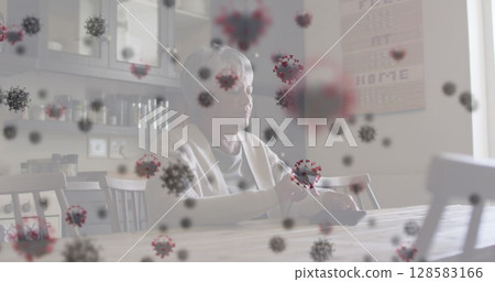 Sitting elderly woman holding handheld device at wooden kitchen table at home, with virus overlays 128583166