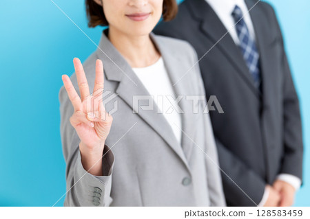 A middle-aged female businesswoman and a male businessman wearing a gray suit holding up three fingers 128583459