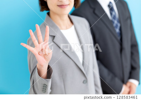 A middle-aged female businesswoman and male businessman wearing gray suits holding up four fingers A middle-aged female businesswoman and male businessman wearing gray suits holding up four fingers 128583461