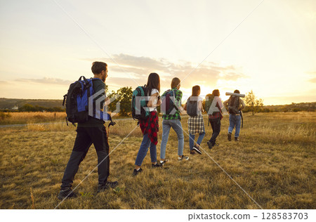 Group of friends tourists trekking with backpacks walking in a row in the field. Group of friends tourists trekking with backpacks walking in a row in the field. 128583703