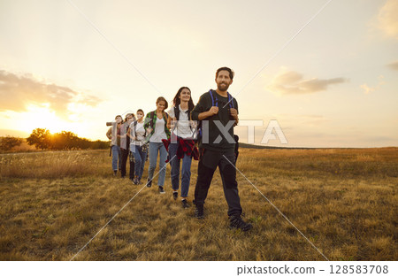 Team of tourists with backpacks walking through field during trekking or hiking tour 128583708