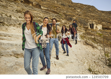 Happy, cheerful friends having fun while walking down rocky mountain trail together 128583709