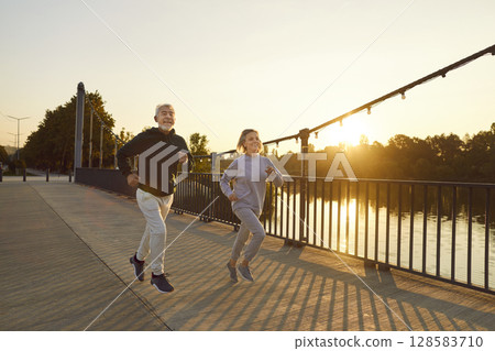 Happy healthy senior couple running along a bridge during a sports workout in the city park 128583710
