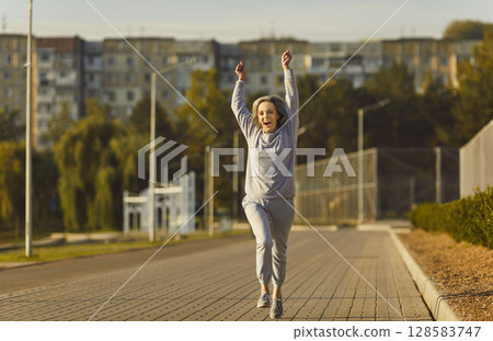 Positive Senior Woman Jogging with a Smile in City Park Positive Senior Woman Jogging with a Smile in City Park 128583747