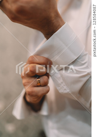A man is getting dressed in a white shirt and is adjusting his shirt sleeves. Concept of formality and attention to detail, as the man is taking the time to properly dress himself A man is getting dressed in a white shirt and is adjusting his shirt sleeves. Concept of formality and attention to detail, as the man is taking the time to properly dress himself 128584087