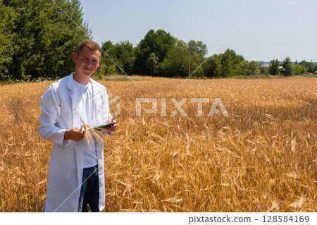 Young agronomist, farmer with tablet in hands, creates yield maps in wheat field Young agronomist, farmer with tablet in hands, creates yield maps in wheat field 128584169